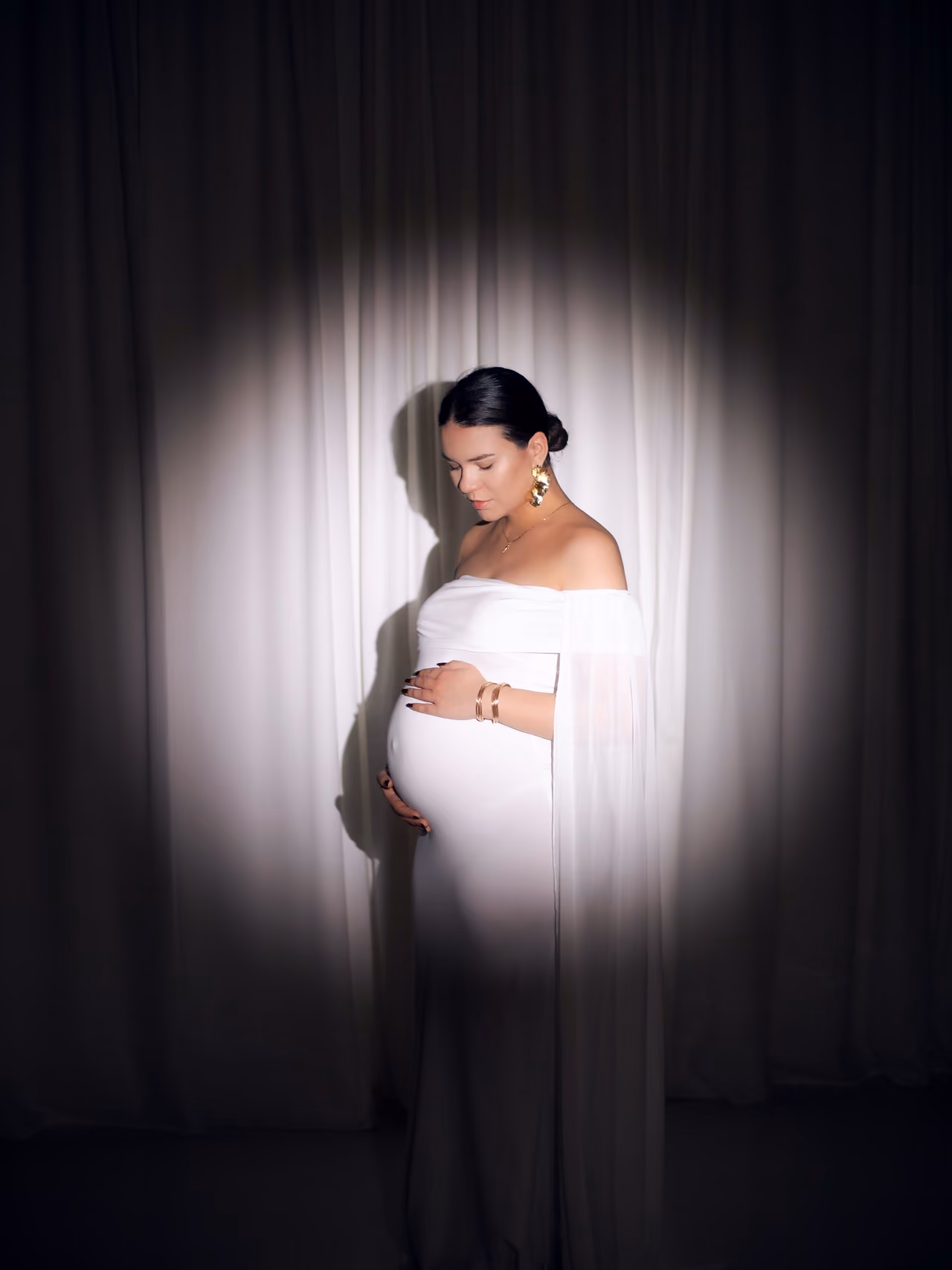 Maternity portrait in a white dress under a spotlight