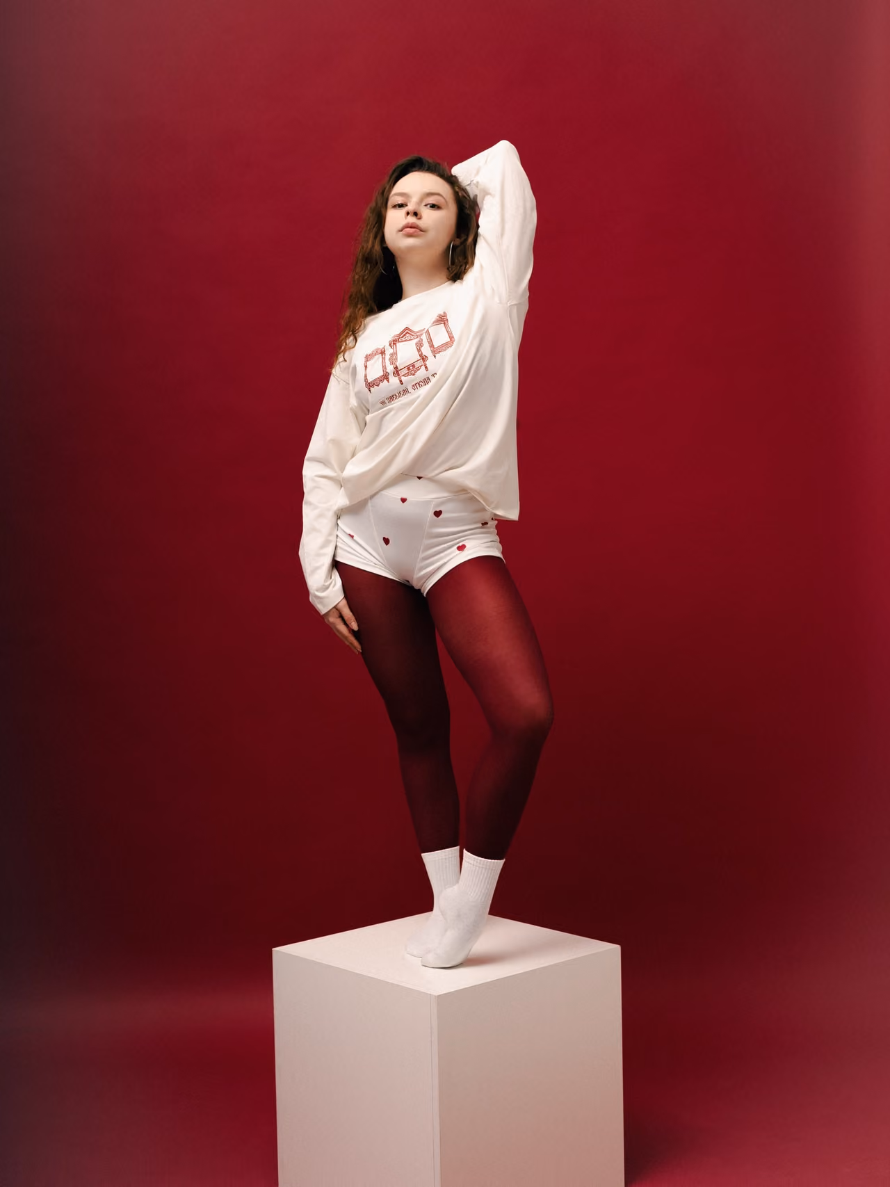 Woman in a white sweatshirt posing on a block against a red backdrop