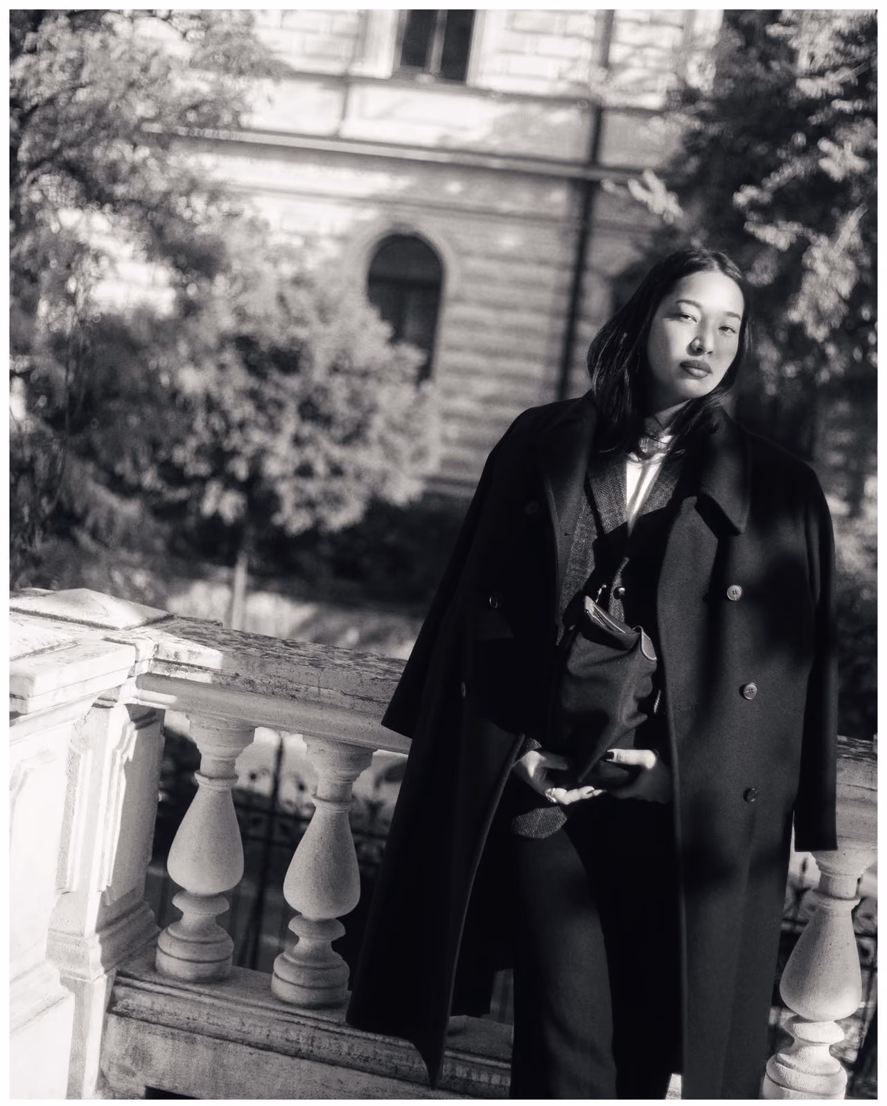 Black and white portrait of a woman in a long coat by a balustrade